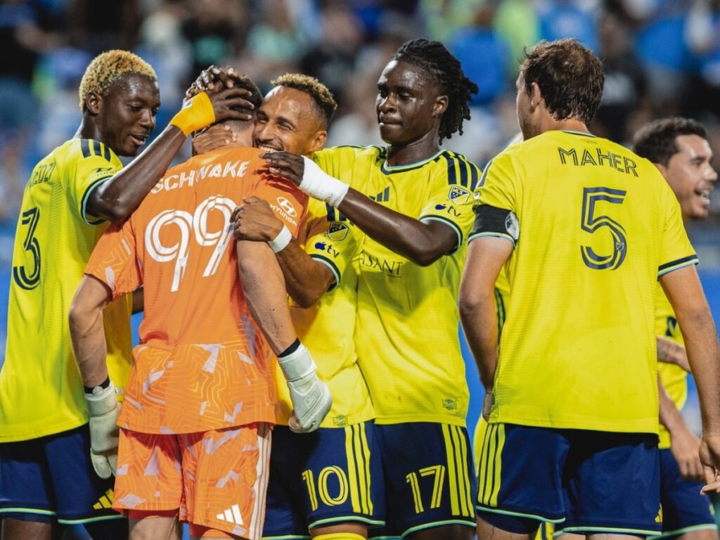 Jugadores de Nashville SC rodean y abrazan a Brian Schwake #99 tras su atajada del penal ante Charlotte FC en el Bank of America Stadium — MLS 2026
