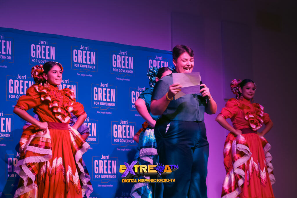 Una estudiante de Middle Tennessee State University habla por un micrófono en el escenario, acompañada de jóvenes con vestidos tradicionales.
