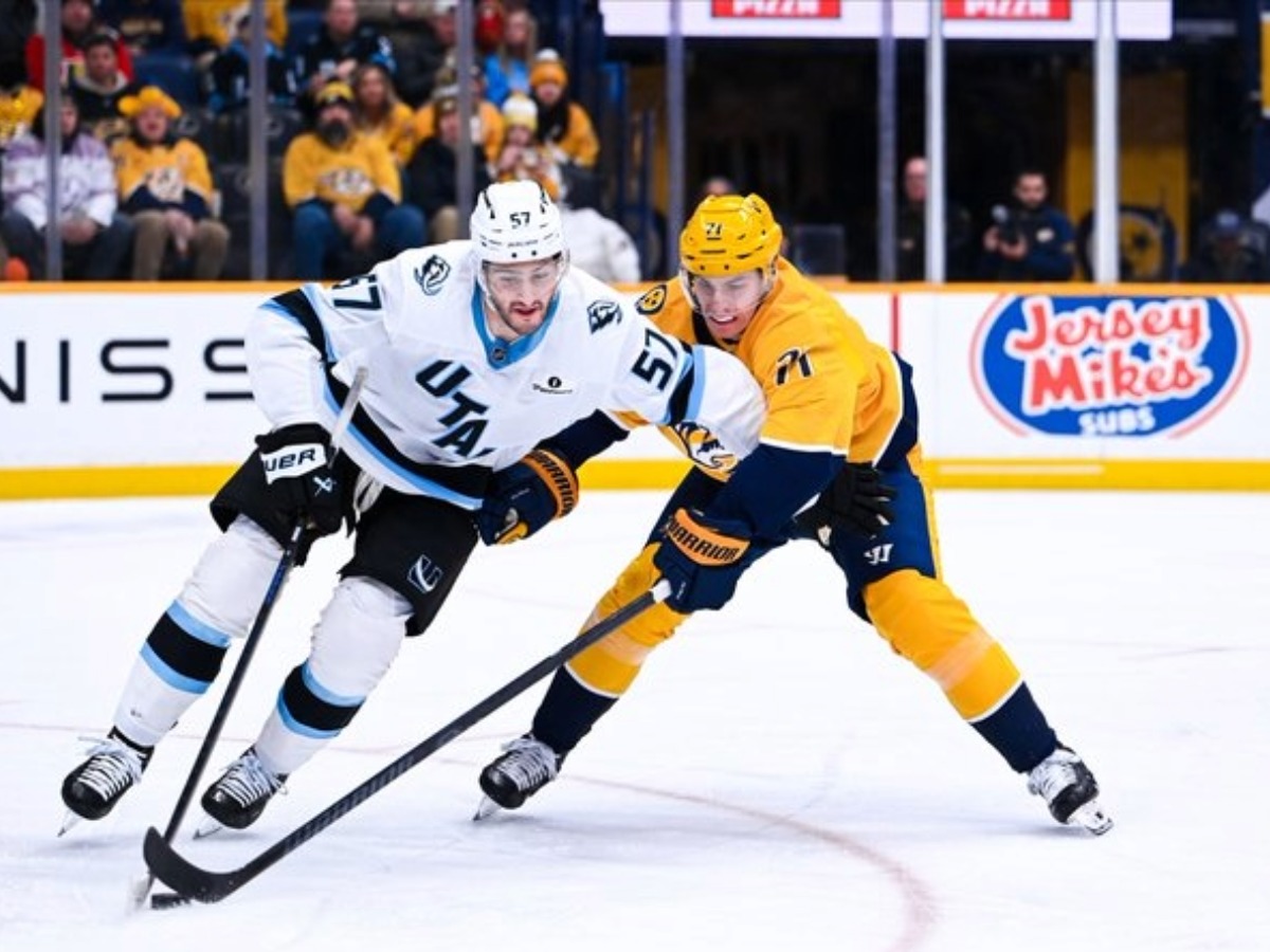 Jugador de Utah Hockey Club protege el disco ante la presión defensiva de Nashville Predators.