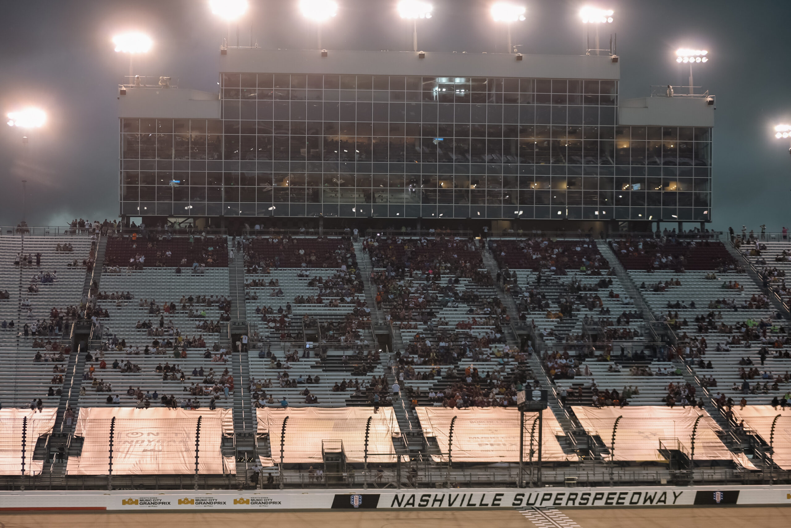 Aficionados resguardándose en la grada principal iluminada del autódromo de Nashville tras la lluvia