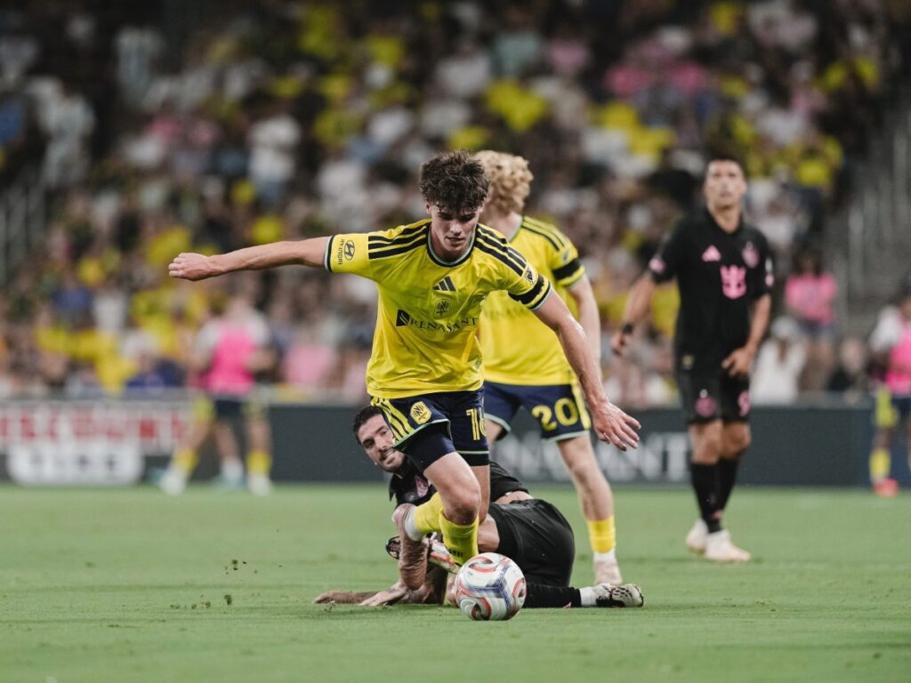 Matthew Corcoran avanza con el balón controlado eludiendo la barrida del rival en la medular