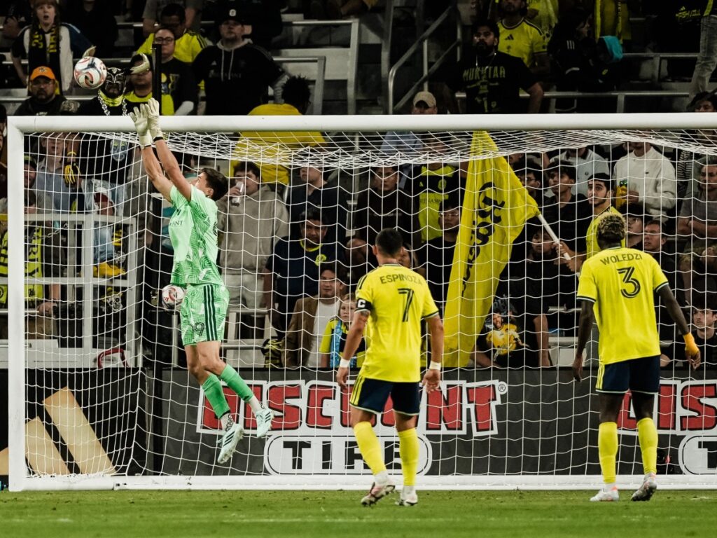 Brian Schwake salta por alto descolgando el balón junto al travesaño con Daniel Lovitz y Maxwell Woledzi custodiando el arco