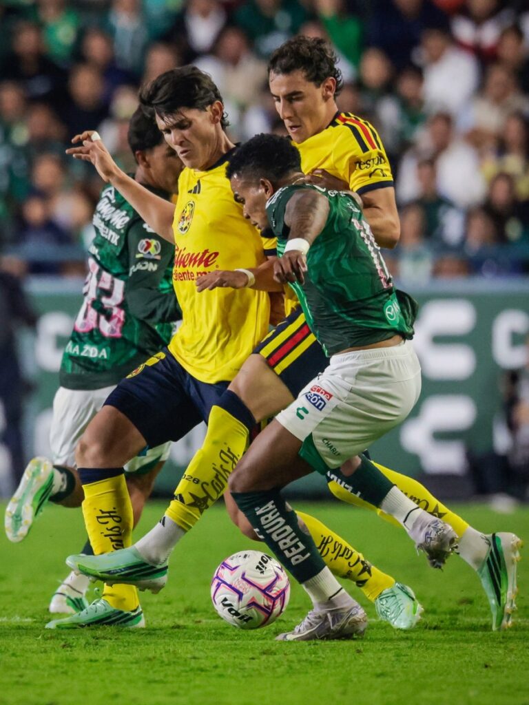Jugadores de América y León forcejean en el centro del campo disputando la posesión
