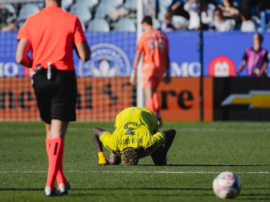 Maxwell Woledzi se arrodilla sobre el césped con la frente en el pasto celebrando el título