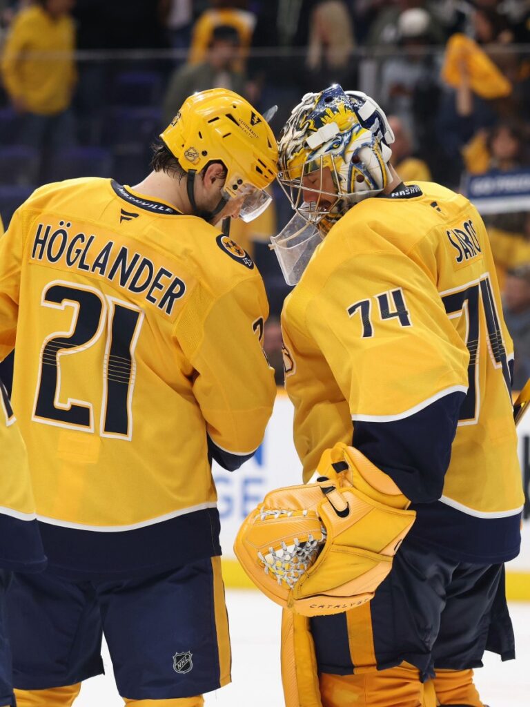 Nils Höglander y Juuse Saros juntan sus cascos al finalizar el partido sobre el hielo